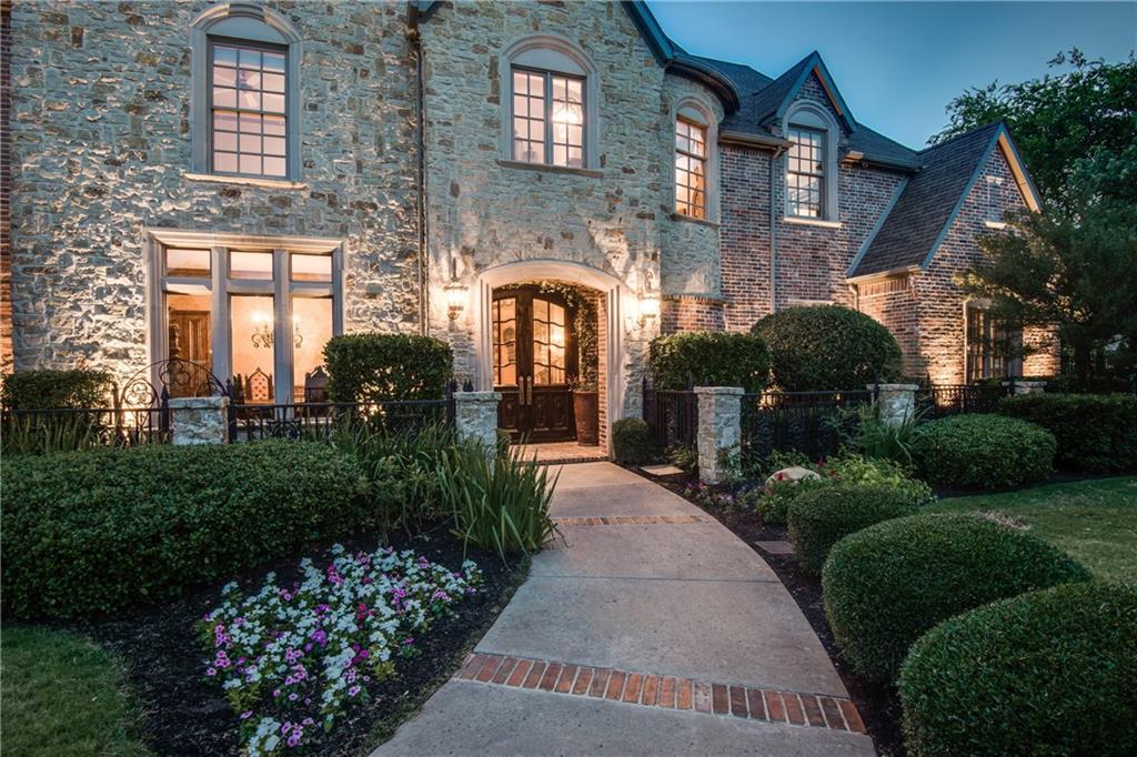 A two story wood home with a steep roof and warm lights on at dusk, with a green lawn and garden in front